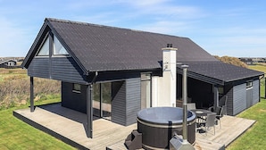 Een modern huis met een jacuzzi, buitenmeubels en een schoorsteen.