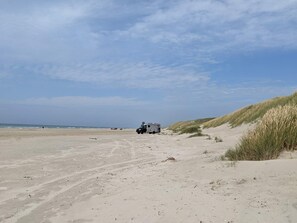Una spiaggia con un buggy fuoristrada parcheggiato sulla sabbia, cielo sereno e l'oceano sullo sfondo.