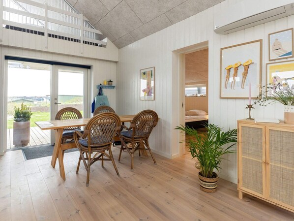 A dining area with a wooden table and chairs, a potted plant, and a wicker cabinet.