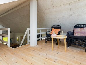 A wooden-floored balcony with two black wicker chairs, a small round table, and a white pillar. - 5 Star Holiday Home in Lokken (Lokken)