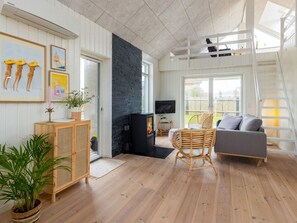 A living room with a fireplace, a grey sofa, a wicker chair, and a television. - 5 Star Holiday Home in Lokken (Lokken)