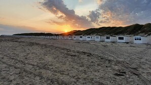 Een rij witte strandhutten met een zonsondergang op de achtergrond.