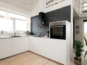 A modern kitchen with white cabinetry, a black stone backsplash, and a built-in oven. - 5 Star Holiday Home in Lokken (Lokken)