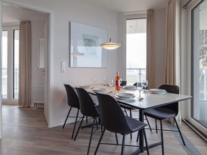 A modern dining area with a table set for four, black chairs, a pendant light, and a bottle of wine.