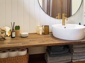 Ein Badezimmer mit einem Holzkosmetikschrank, einem weißen Waschbecken, einem goldenen Wasserhahn, einem runden Spiegel und einer Topfpflanze.