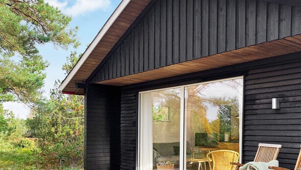 Een modern huis met een houten terras, grote schuifdeuren en tuinmeubilair.