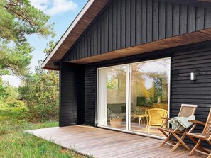 A modern house with a wooden deck, large sliding glass doors, and outdoor furniture. - 7 Person Holiday Home in Laeso (Læsø)