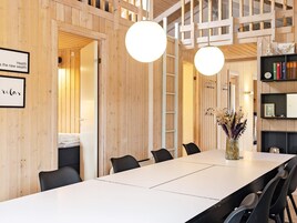 Un interior moderno con una larga mesa de comedor, sillas negras, paredes de madera y una escalera.