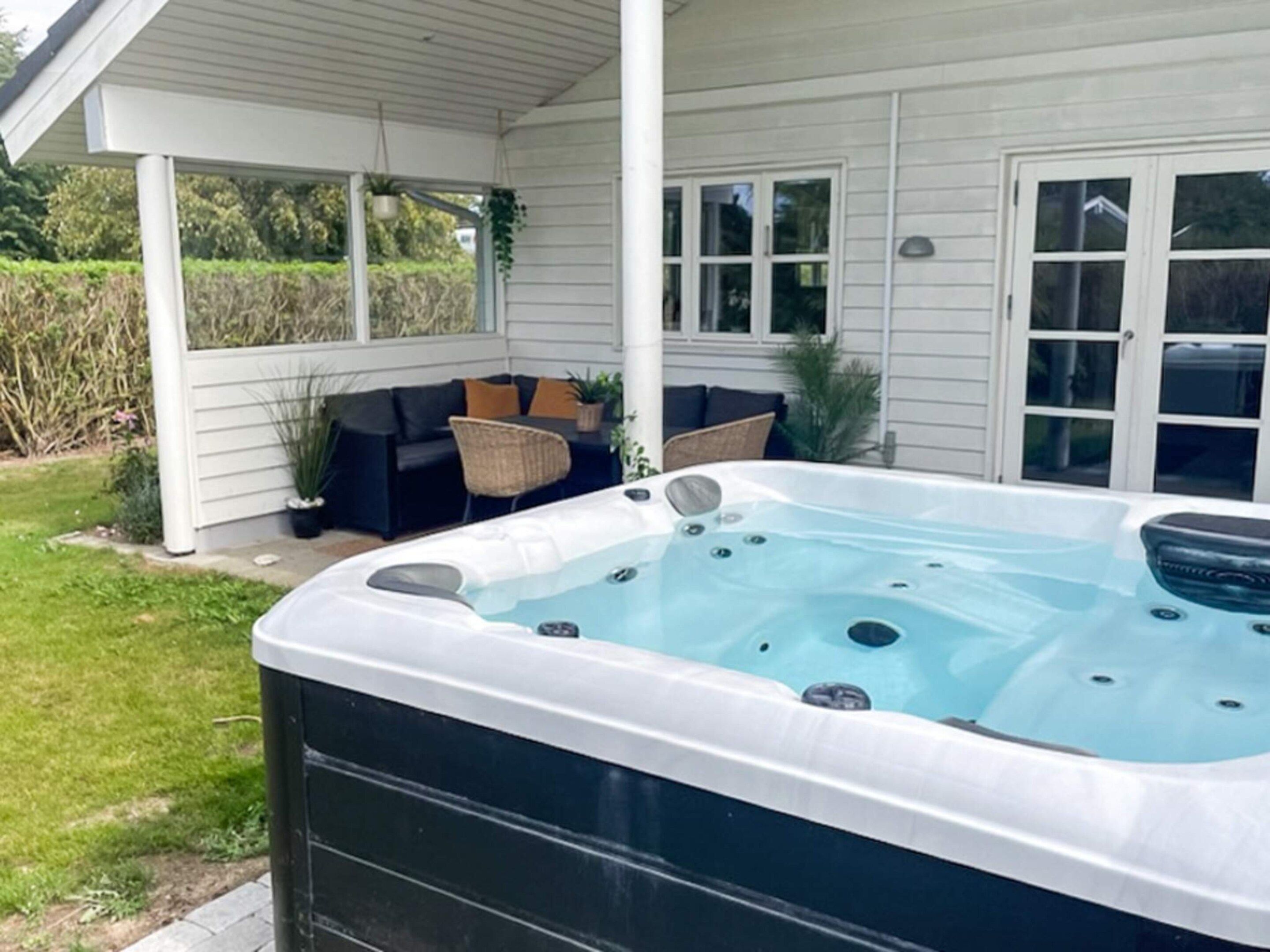 A hot tub in a covered outdoor area with a patio, seating, and a view of the surrounding landscape.