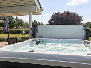 An outdoor hot tub with a covered seating area, surrounded by a garden and a swing set.