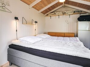 A bedroom with a bed, wooden headboard, white walls, and a ceiling with wooden beams.
