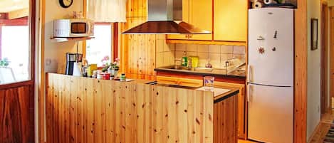 A compact kitchen with wooden cabinetry, a microwave, a stove, and a refrigerator.