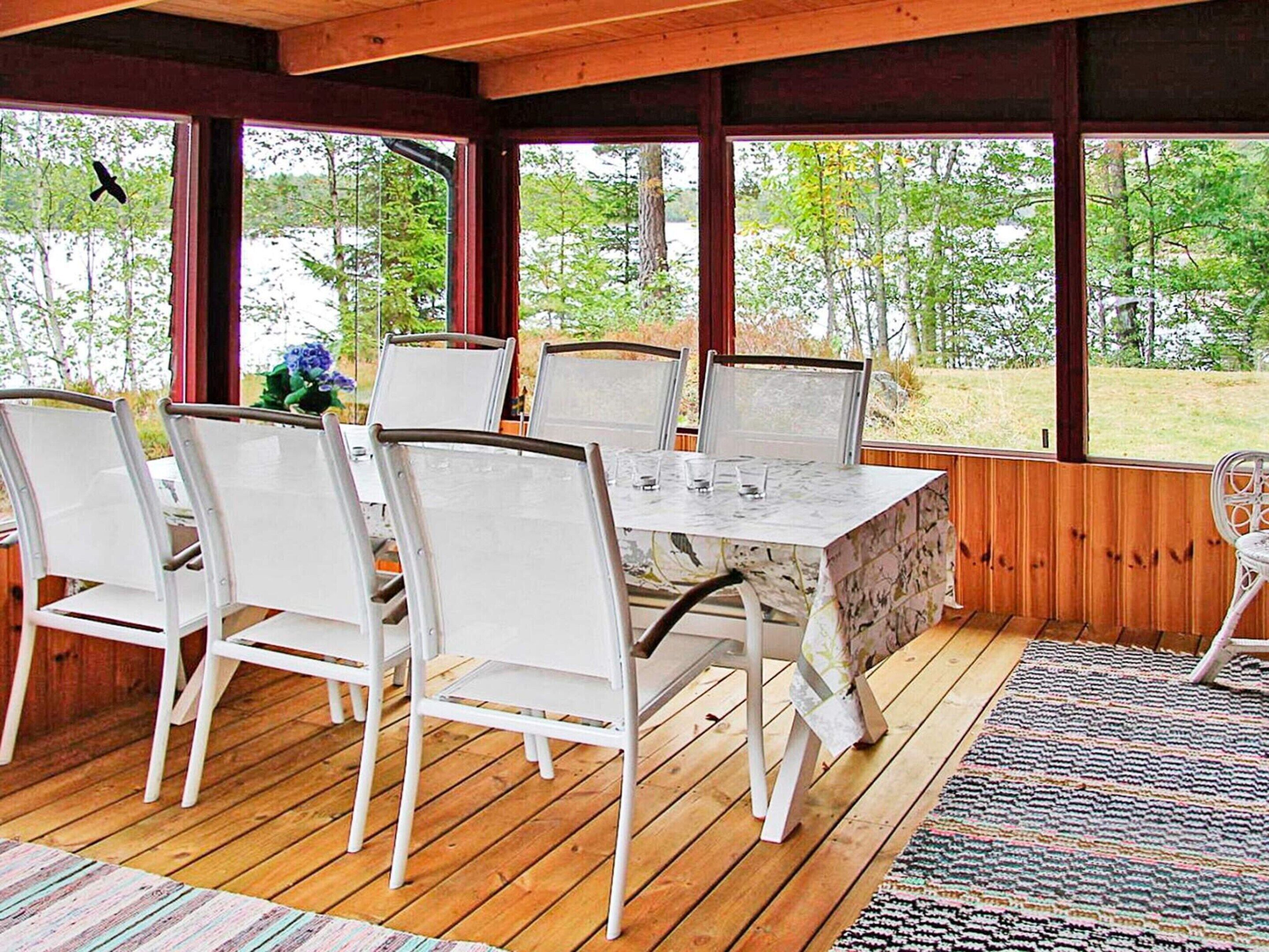 A covered outdoor dining area with a table and chairs, large windows, and a view of trees.