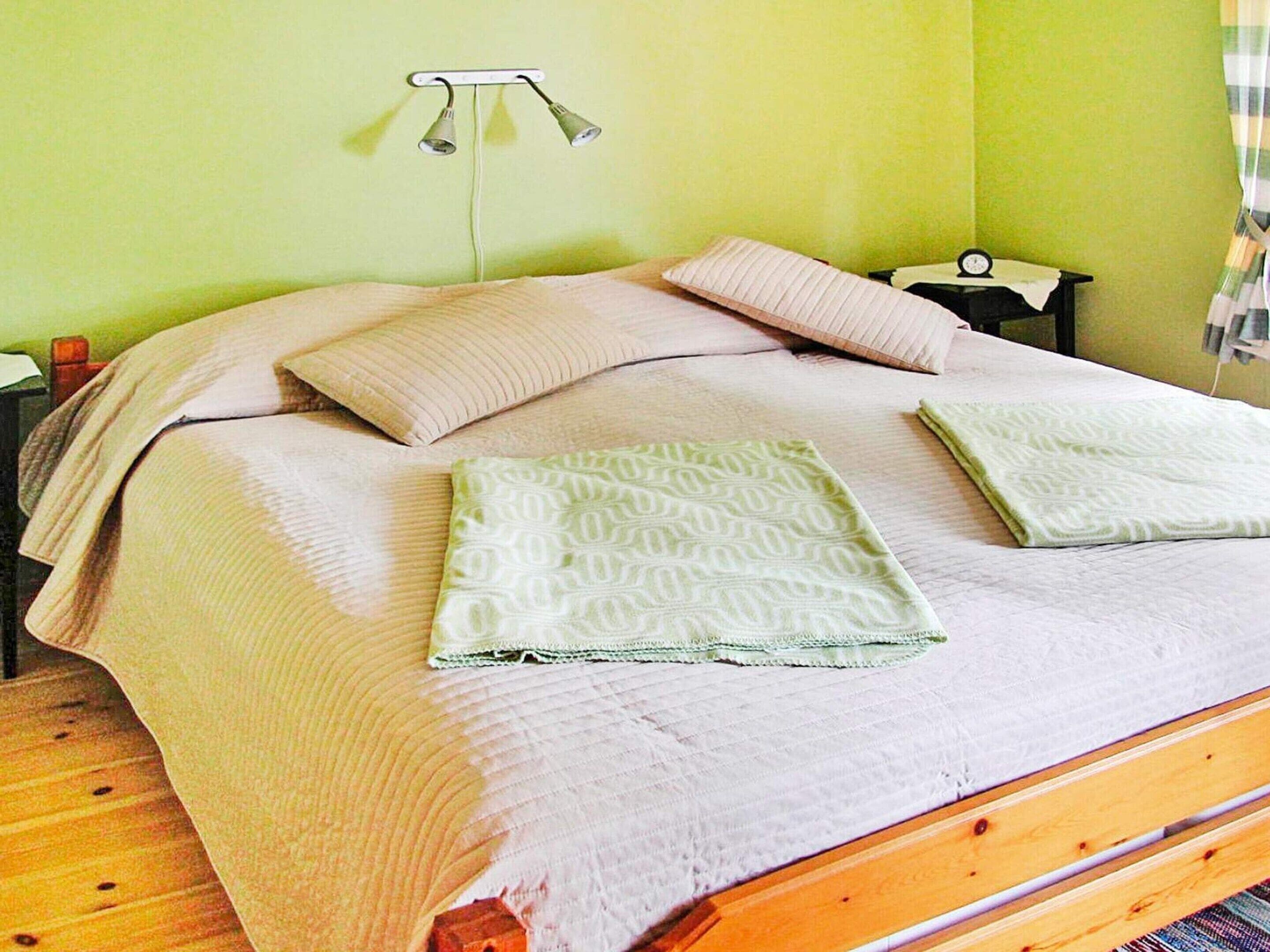 A bed with a wooden frame, two pillows, a blanket, and a bedside table with a lamp.