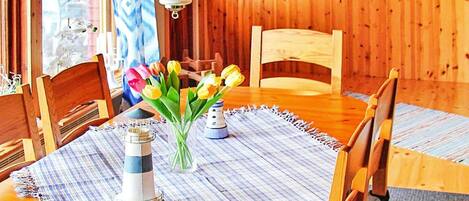 Une table à manger en bois avec des chaises, un vase de tulipes, un salière en forme de phare et une nappe à rayures.