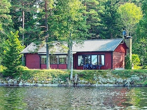 A red cabin by a lake with a dock, surrounded by trees.