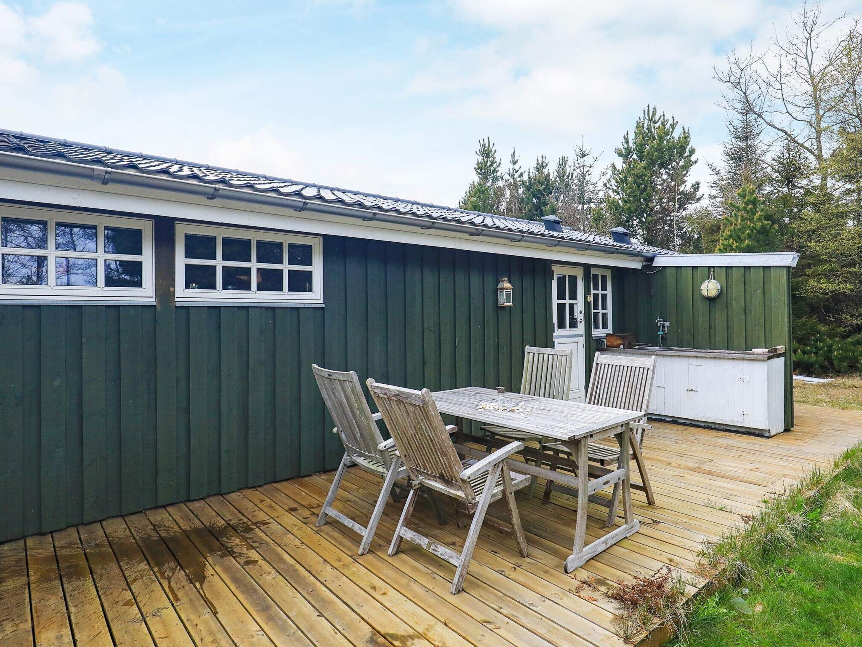 A wooden deck with a table and chairs, a small shed, and a green building with windows and a door.