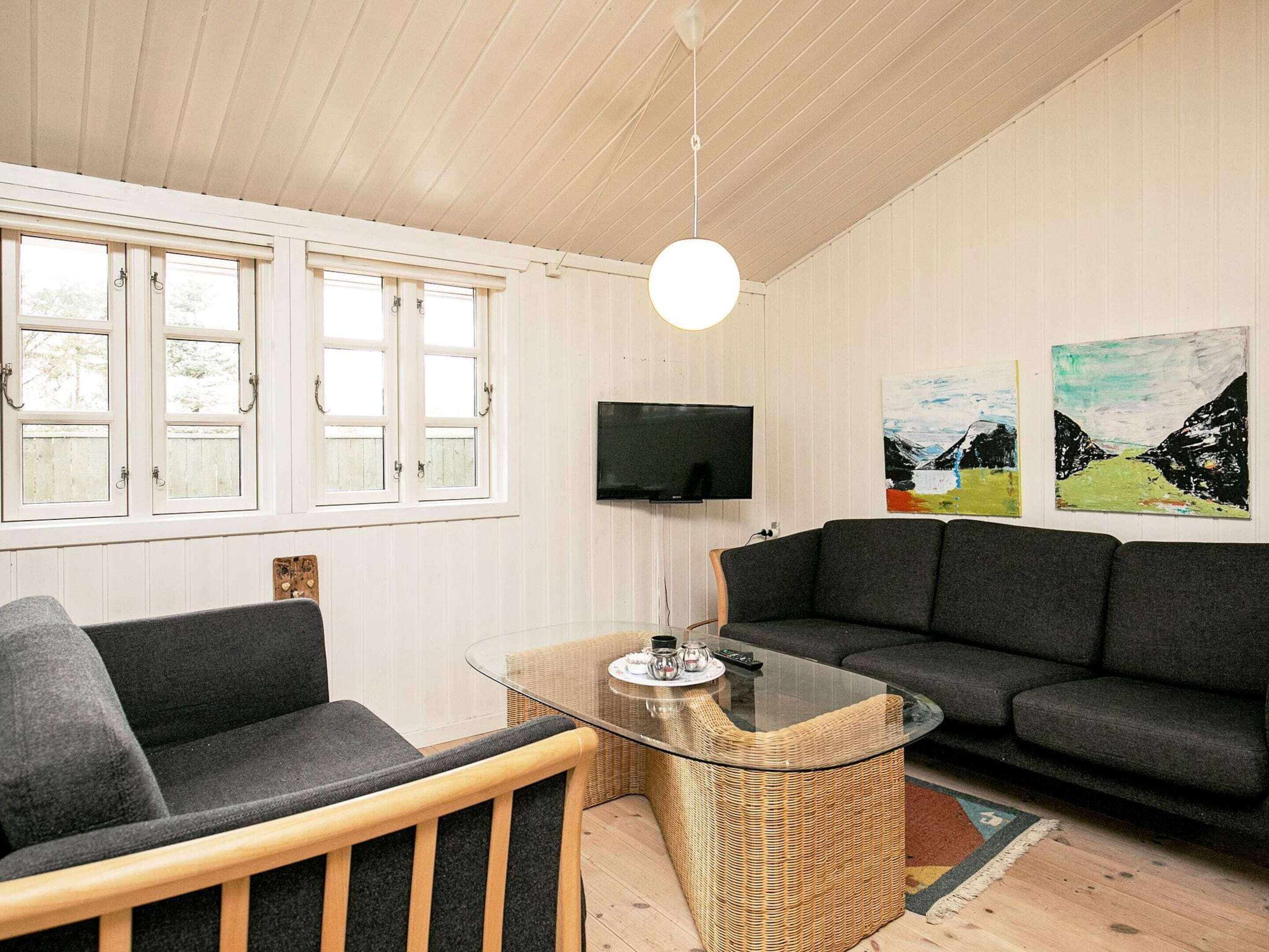 Ein modernes Wohnzimmer mit einem Glastisch, einem dunkelgrauen Sofa und einem an der Wand befestigten Fernseher.