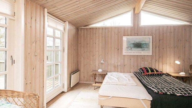 A cozy room with a wooden ceiling, a bed with a black and white checkered blanket, a wicker chair, and a framed picture on the wall. - 6 Person Holiday Home in Jerup (Jerup)