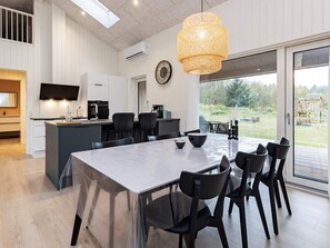 A modern kitchen with a dining area, large windows, and a view of the outdoors.