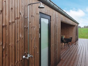 Ein Holzhaus mit Tür, Dusche und einer Terrasse mit Stühlen.