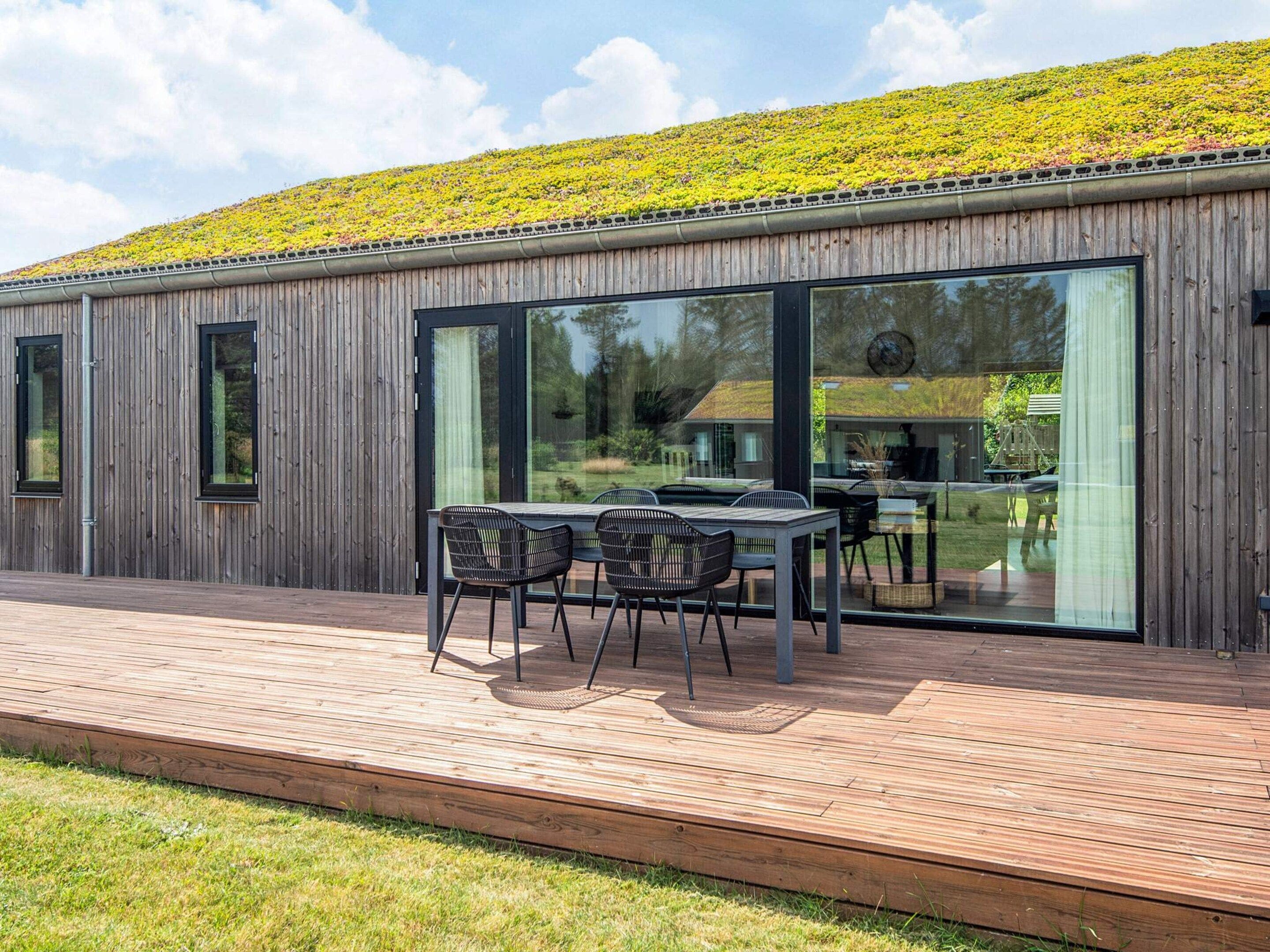 A modern building with a wooden exterior, large glass windows, and a deck with outdoor furniture.
