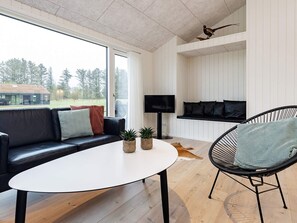 Ein modernes Wohnzimmer mit einem schwarzen Ledersofa, einem weißen Couchtisch, einem schwarzen Korbstuhl und einem Flachbildfernseher an einer weißen Wand.
