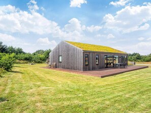 A modern wooden house with a flat roof, large windows, and a deck.