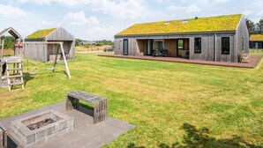 Una casa moderna con tetto verde, un pontile in legno e un braciere nel giardino.