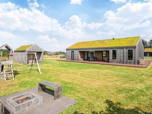 A modern house with a green roof, a wooden deck, and a fire pit in the yard. - 5 Star Holiday Home in Saltum (Saltum)