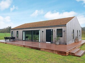 A modern wooden building with large sliding glass doors, a deck, and outdoor seating. - 5 Star Holiday Home in Saltum (Saltum)