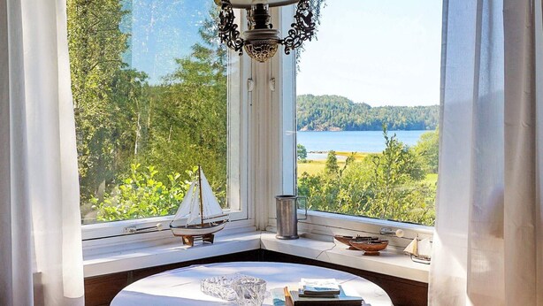 Habitación de esquina con una mesa, una maqueta de un pequeño velero y vistas a un lago.