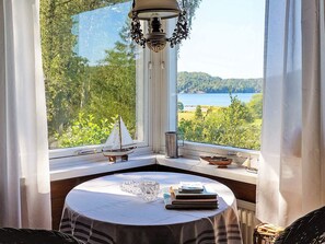 Ett hörnrum med ett bord, en liten modell av en segelbåt och utsikt över en sjö.