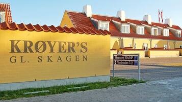 En gul bygning med skilt 'KROYER'S GL. SKAGEN', et belagt område og en skilt med henvisning til 'Højensvej 30A-34P' og 'Vandrestien 7-12'.