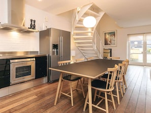 A modern kitchen with a built-in oven, a stainless steel refrigerator, and a wooden dining table with chairs. - 4 Star Holiday Home in Skagen (Skagen)