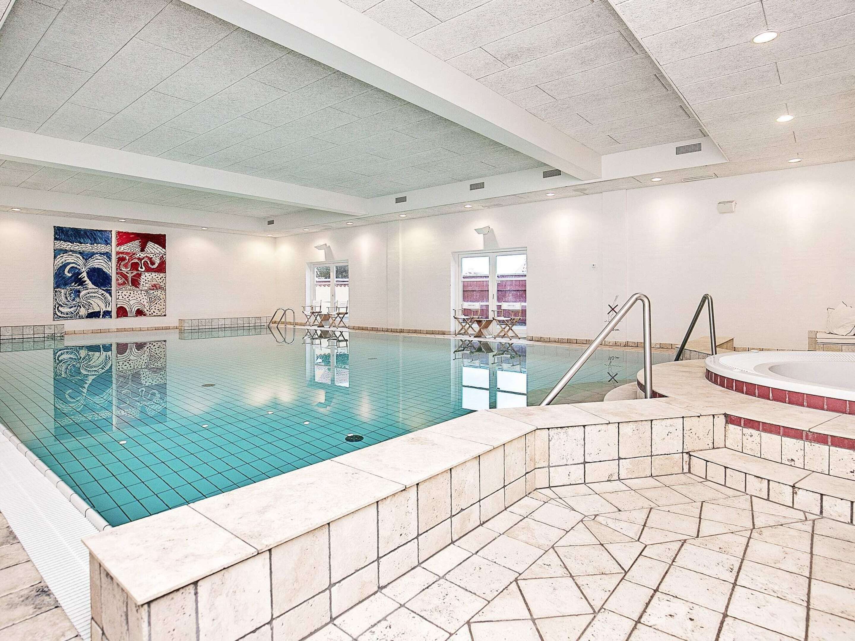 An indoor swimming pool with a clear water surface, a hot tub, and a tiled floor.