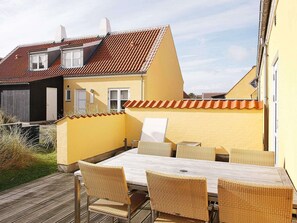 A patio with a table and chairs, a yellow wall, and a red-tiled roof. - 4 Star Holiday Home in Skagen (Skagen)