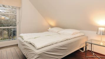 Makuuhuoneessa on sänky, yöpöytä lampun kanssa, ikkuna, josta on näkymä, ja puulattia.