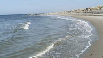 A beach with gentle waves, a sandy shore, and a rocky outcrop in the distance.