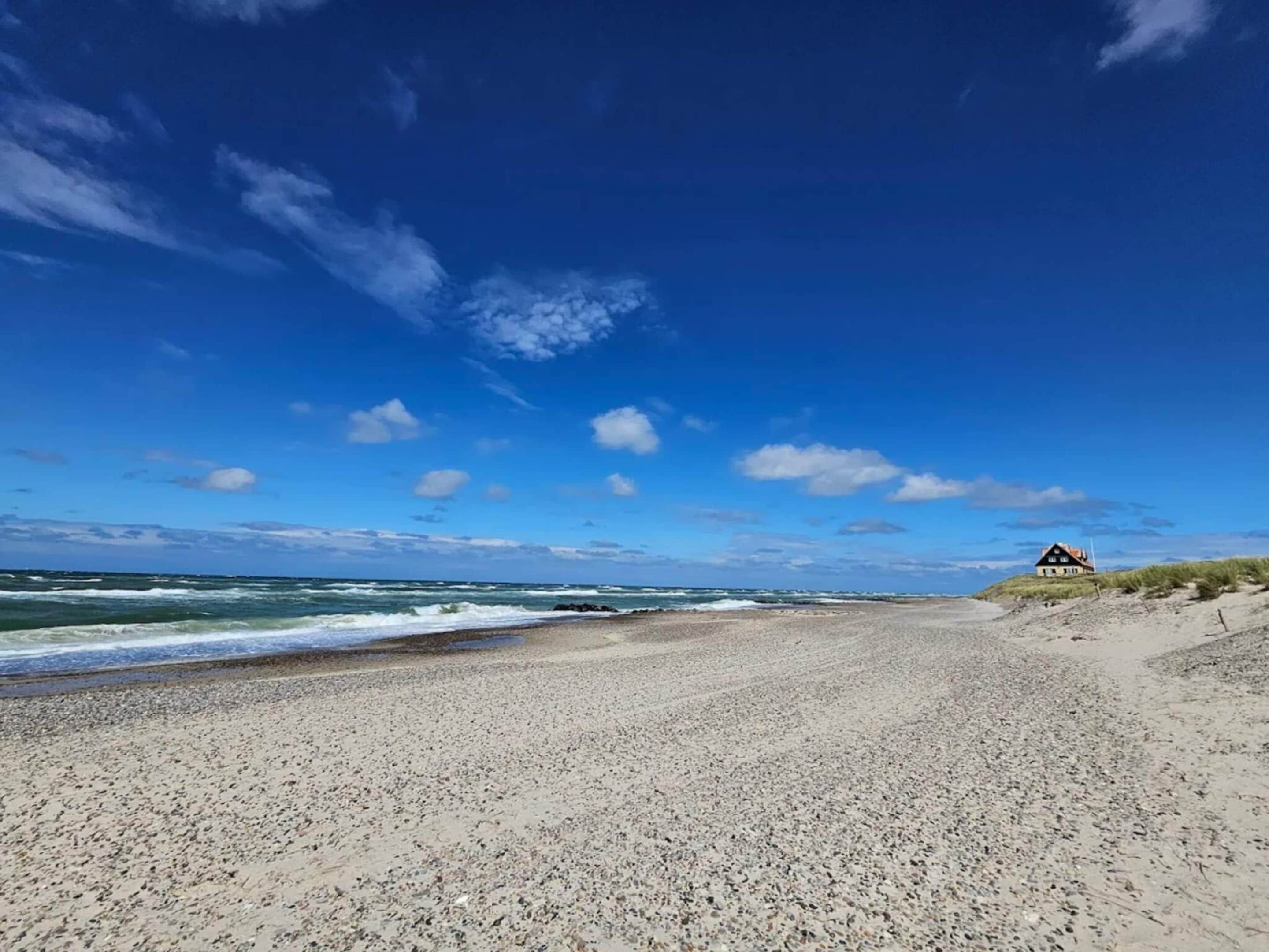 A beach with a house on a dune, waves crashing, and a clear sky.