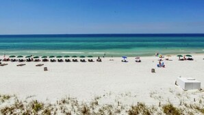 A beach with rows of beach chairs and umbrellas, a white building, and the ocean in the background. - BEACHfront 2-bedroom condo! (Panama City Beach)