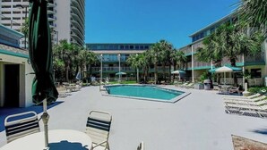 A pool area with lounge chairs and umbrellas, surrounded by buildings and palm trees. - BEACHfront 2-bedroom condo! (Panama City Beach)