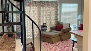 A living room with a spiral staircase, a sofa, a coffee table, and a patterned rug. - BEACHfront 2-bedroom condo! (Panama City Beach)