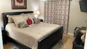 A bedroom with a bed, a ceiling fan, a patterned curtain, and a framed picture on the wall. - BEACHfront 2-bedroom condo! (Panama City Beach)
