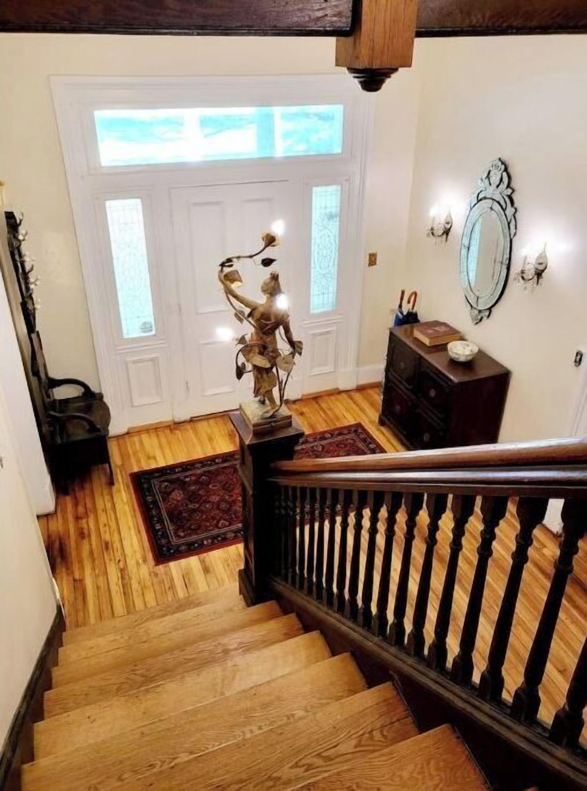 A wooden staircase leading to a white door with a window. A decorative metal sculpture is on the floor beside the door.
