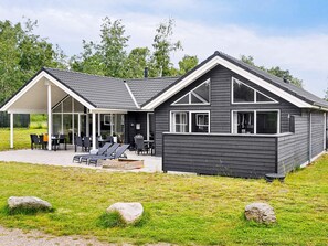 A modern two-story house with a covered patio area, a barbecue setup, and a grassy lawn with rocks. - 5 Star Holiday Home in Vaeggerlose (Vaeggerlose)