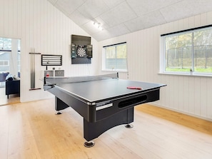 A ping pong table in a room with wooden flooring, white walls, and a window. - 5 Star Holiday Home in Vaeggerlose (Vaeggerlose)