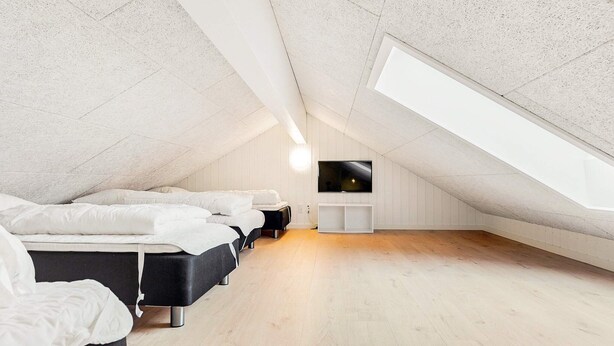 Un dormitorio moderno en el ático, con techo inclinado, suelo de madera y televisor montado en la pared.