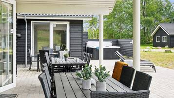 An outdoor patio with a table and chairs, a hot tub, and a covered seating area.