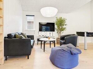 En moderne stue med sofa, puf, fjernsyn og en plante.